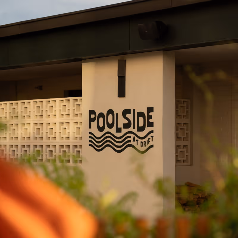 Poolside at Drift sign painted on a beige concrete pillar with decorative breeze block walls and greenery in the foreground.