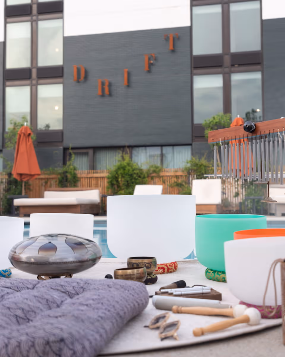 Sound healing instruments including crystal singing bowls, a handpan, and chimes arranged poolside at the Drift hotel.