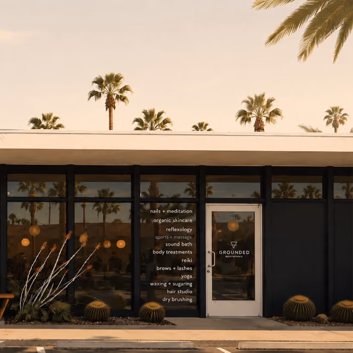 Grounded Bodyworks storefront with palm trees, barrel cacti, and services listed on the window including massage and yoga.
