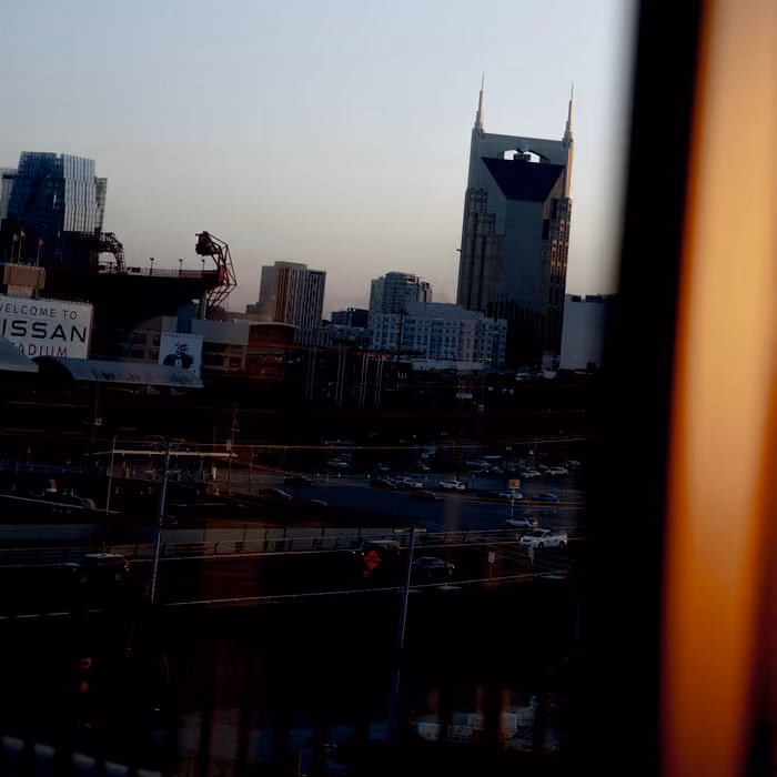 Nashville skyline at dusk featuring the AT&T Building and Nissan Stadium sign viewed from a bridge