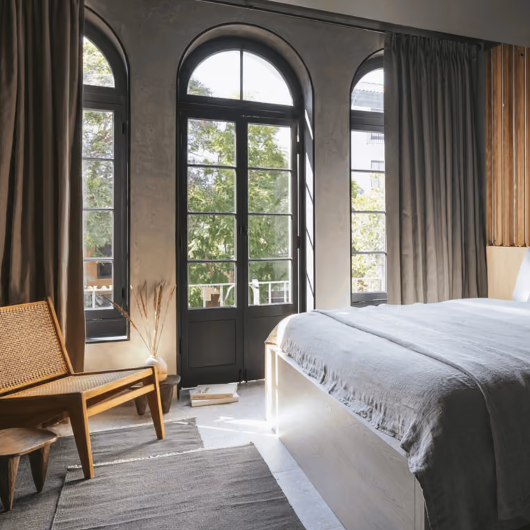A hotel room with a bed, chair, and windows showing an outdoor view.