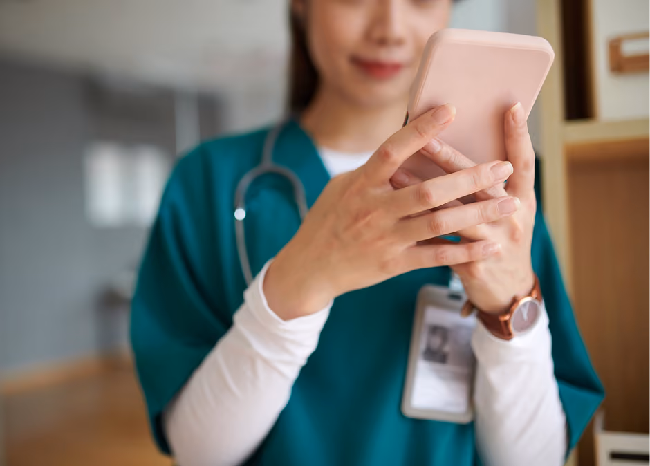 Healthcare professional in green scrubs with a stethoscope around her neck using a smartphone, with focus on her hands and phone.