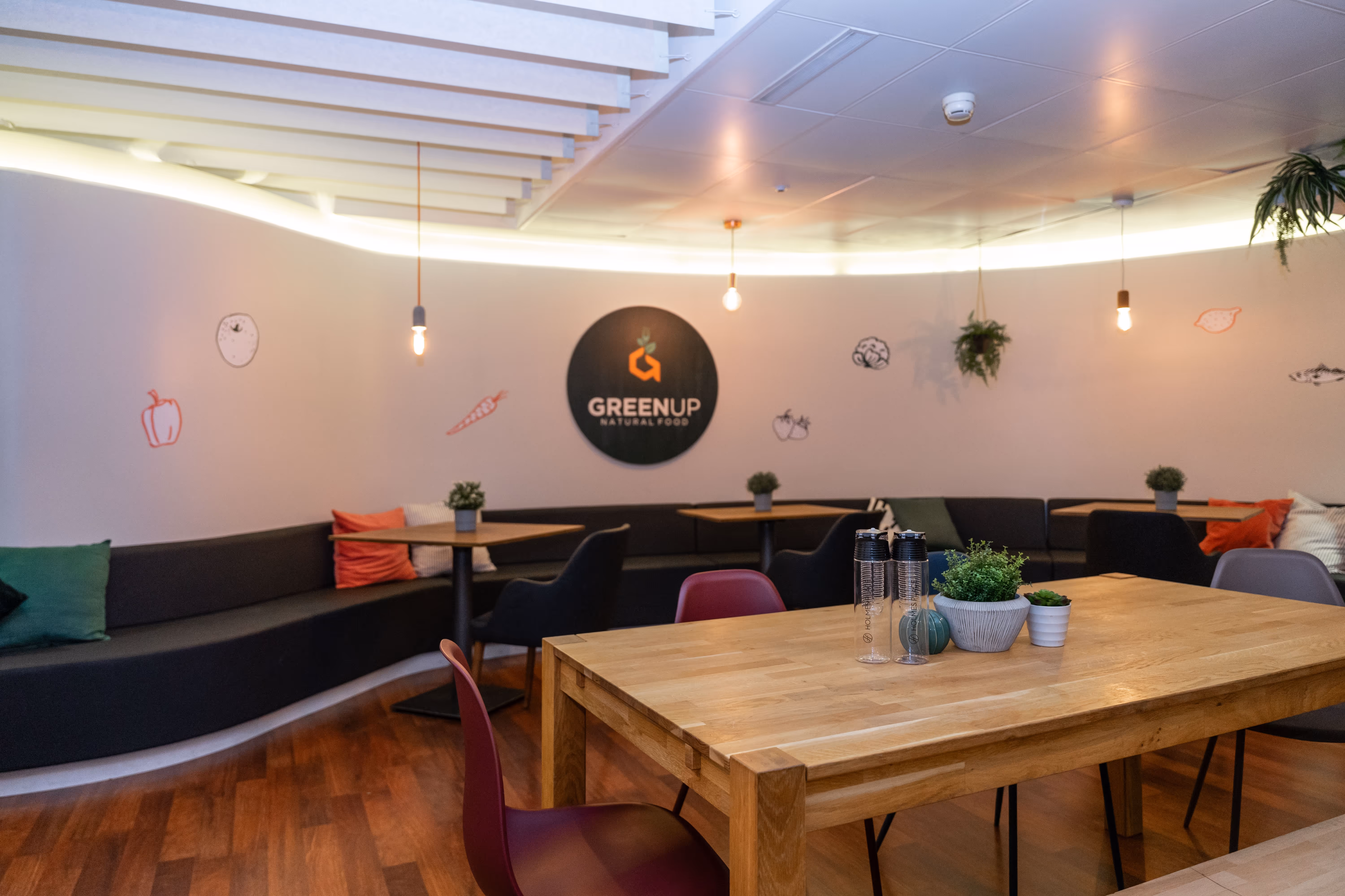 Gemütlicher Essbereich mit Holztisch, bunten Stühlen und gesunden Greenup-Speisen in der Nähe