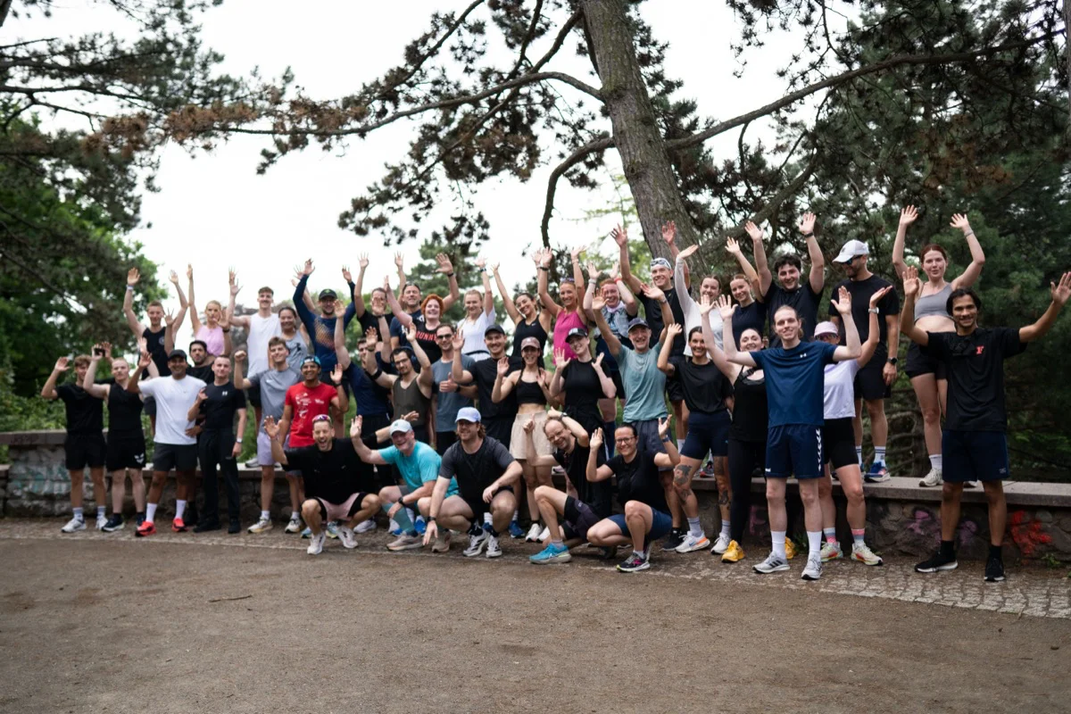 Community von Läufer:innen, die sich für ein Gruppenfoto vor Bäumen versammelt haben und jubeln

