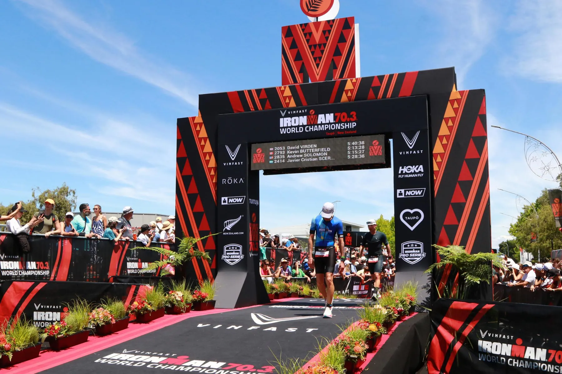 Triathlet:innen laufen auf den Zielbogen zu
