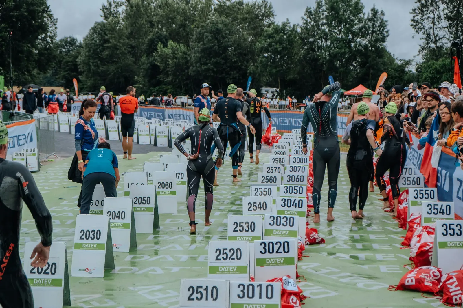 Triathlet:innen in Neoprenanzügen warten in Startboxen auf den Schwimmstart