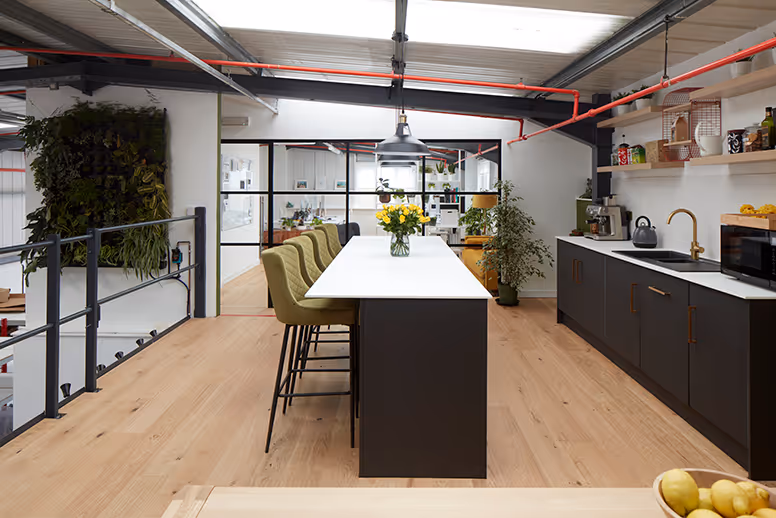 Modern office kitchen with long table, green chairs, and industrial design