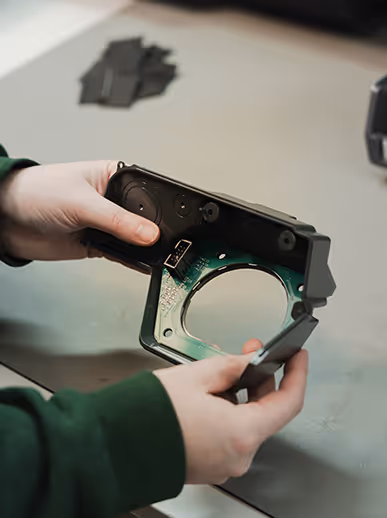 Hands holding a black mechanical device with green circuit board