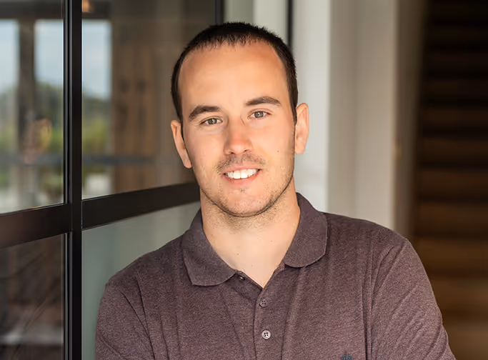 Smiling professional in brown polo shirt standing near glass window
