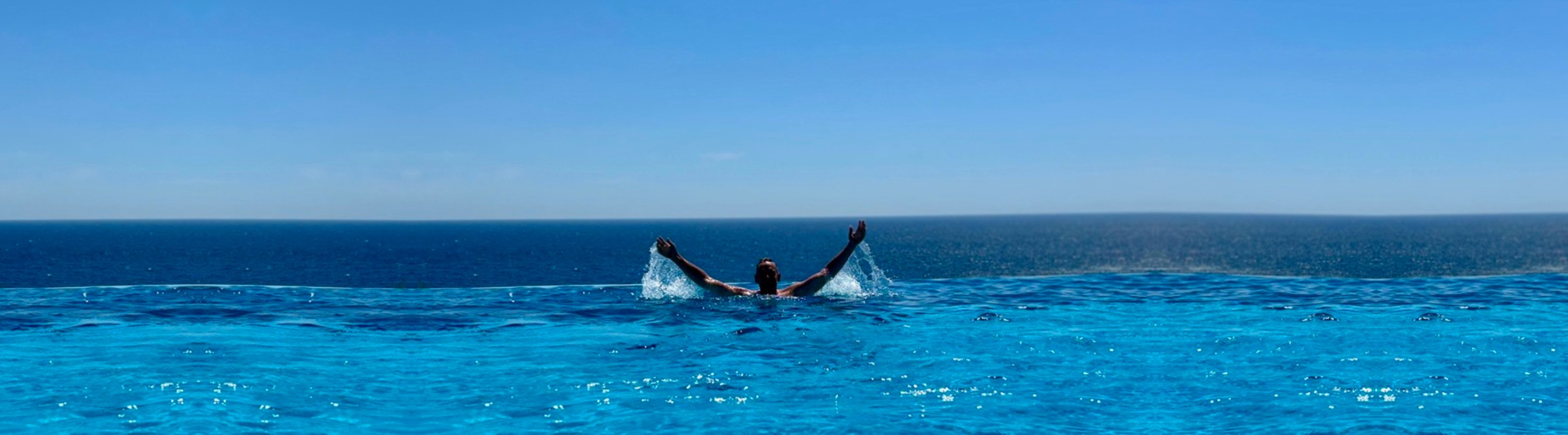 Dennis Rehm im Infinity-Pool mit Blick aufs Meer, die Arme in die Luft gestreckt