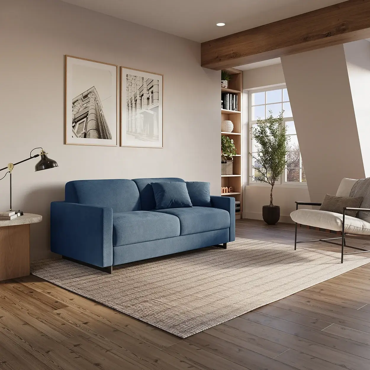 Modern living room with a blue fabric sofa with two matching cushions on a beige rug, a light wooden side table with a black adjustable lamp and books, two black and white architectural photos framed on the wall, a beige armchair with gray cushions, a large window letting in natural light, a potted plant, and built-in wooden shelves with decor items.