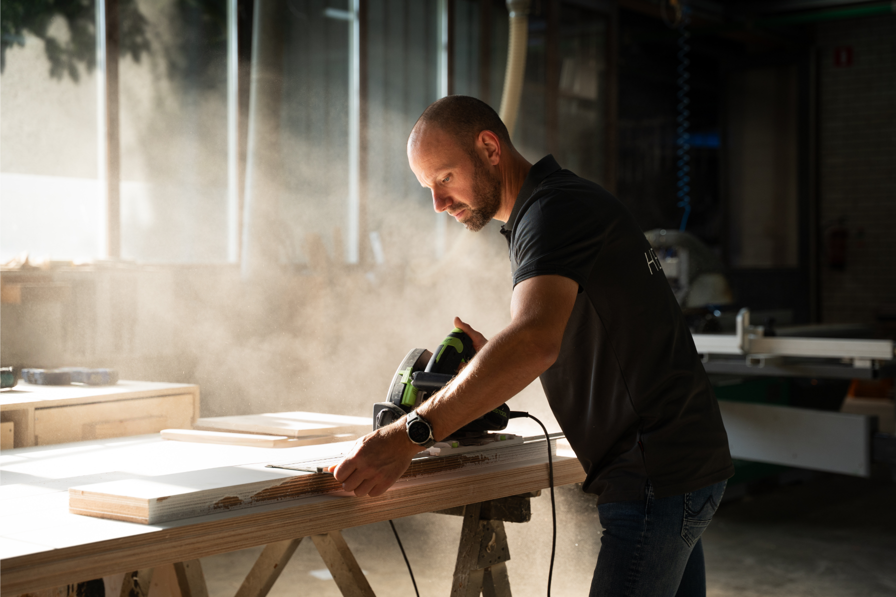 Carpenter sanding wood in a dusty, sunlit workshop.
