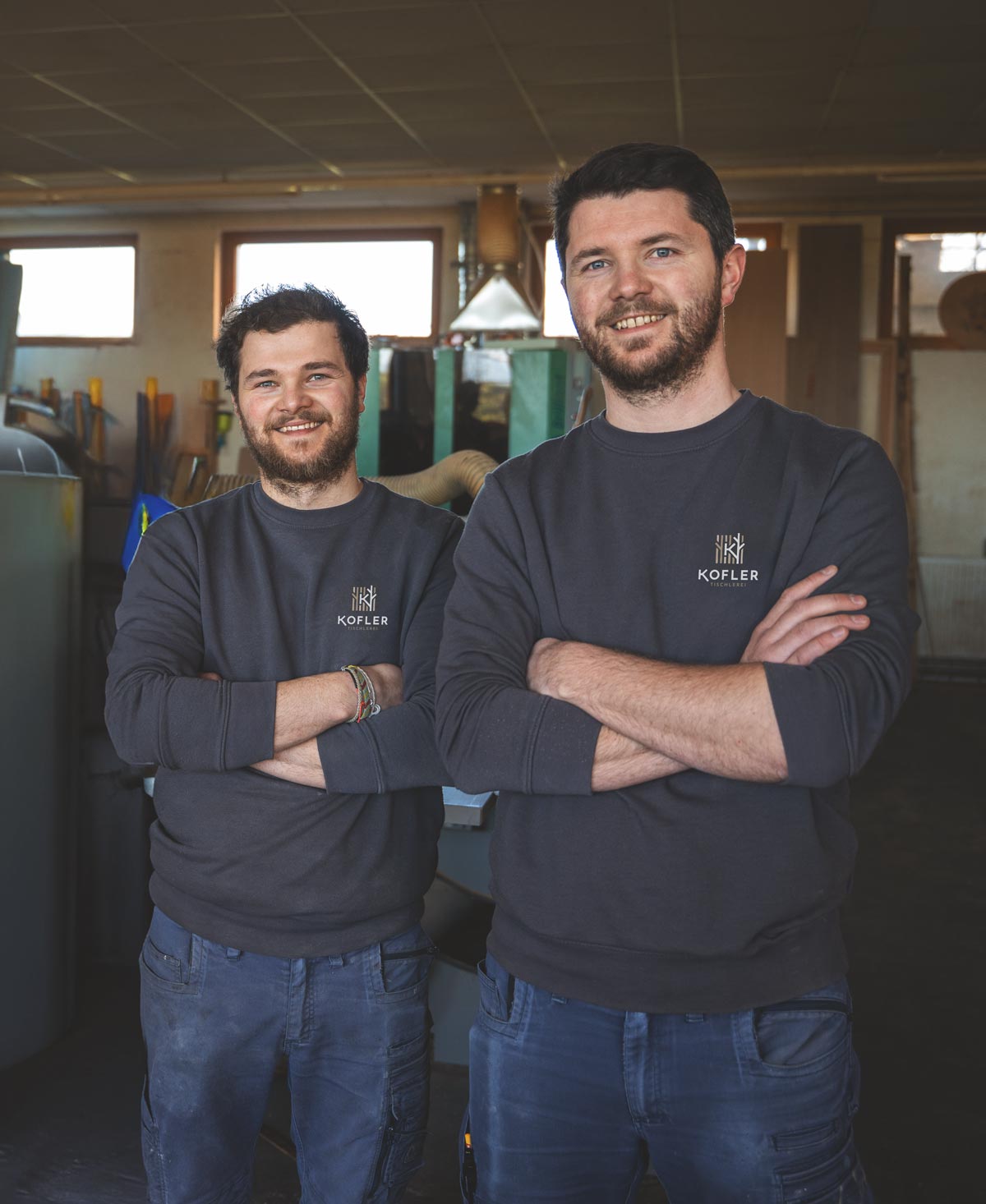 Die 2 Brüder, Josef und Johannes der Tischlerei Kofler, stehen gemeinsam im Werkraum und strahlen Freude und Kompetenz aus.