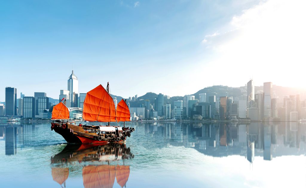 Red junk boat crossing Hong Kong harbor with skyline in the background