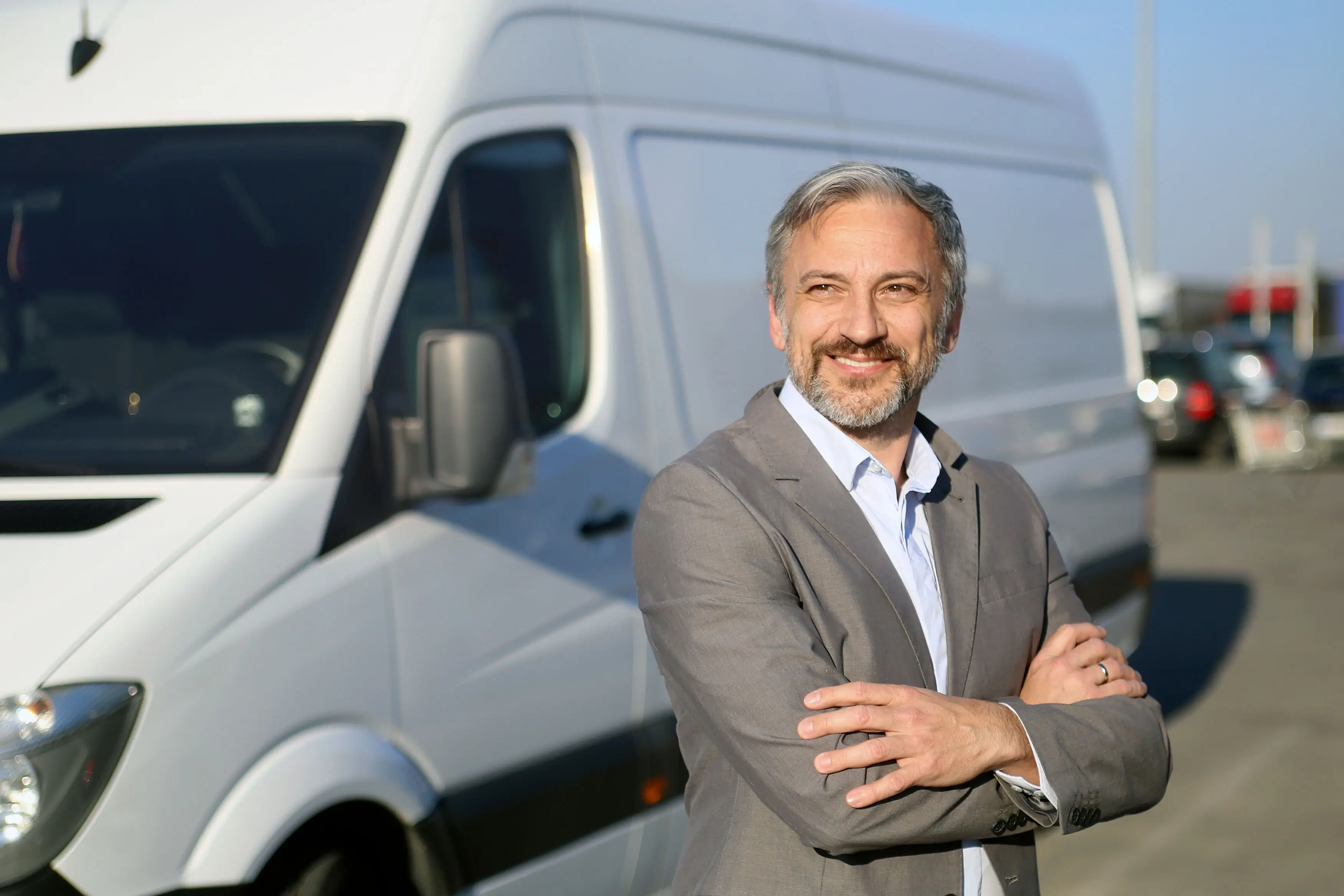 Homme d'âge moyen souriant, bras croisés, debout devant un fourgon blanc garé.
