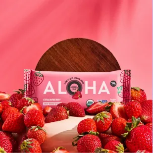 ALOHA strawberry plant-based protein bar surrounded by fresh strawberries.