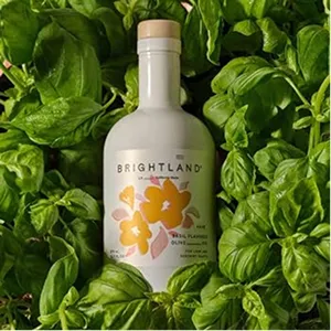 Bottle of Brightland basil-infused olive oil resting on fresh basil leaves.