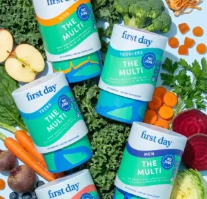 First Day vitamin bottles surrounded by fresh vegetables.