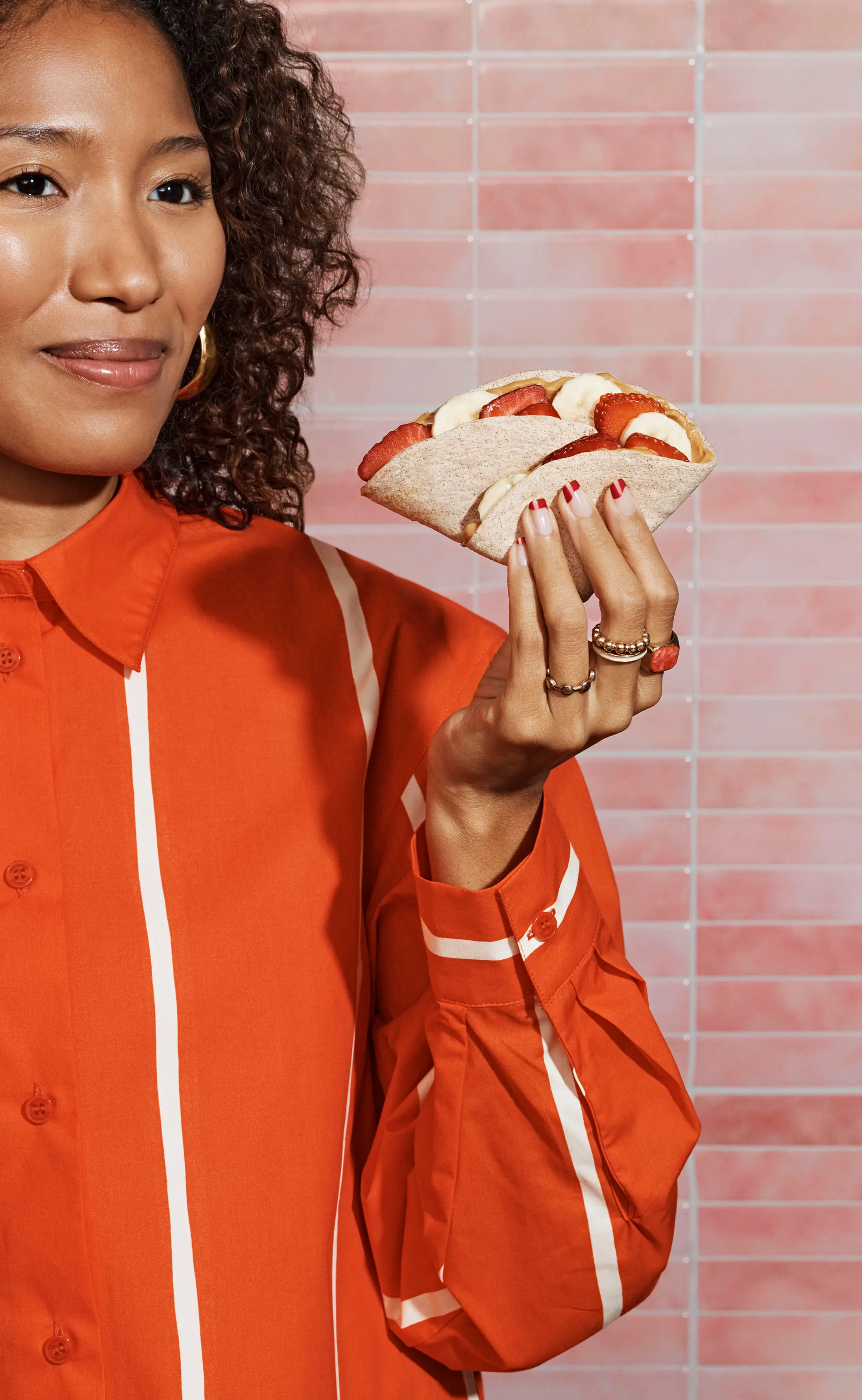Woman in an orange shirt holding a pita stuffed with sliced bananas and strawberries.