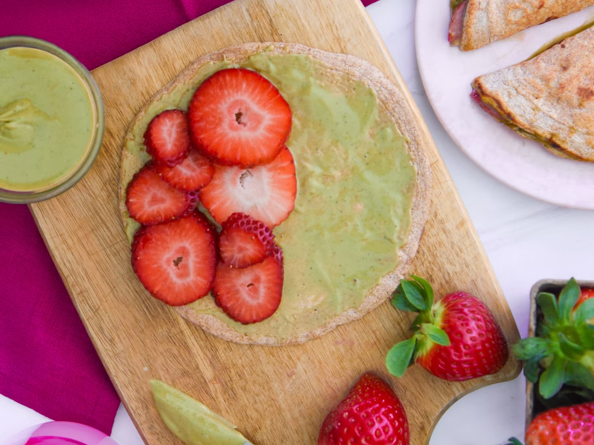 A close-up view of an Egglife wrap assembly, featuring pistachio butter spread and fresh strawberry slices.