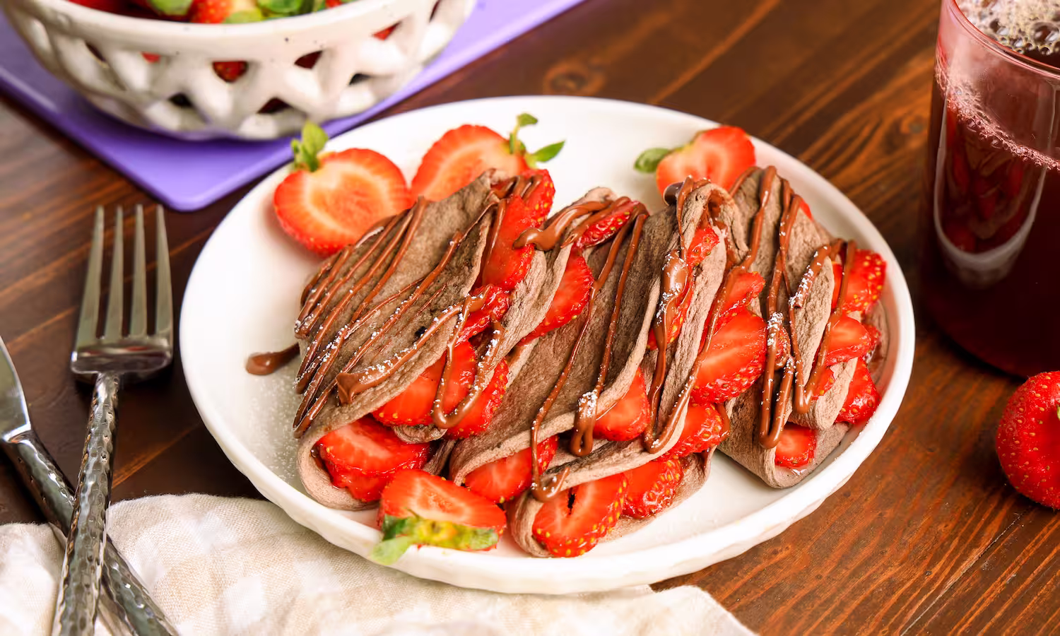 Chocolate egglife wraps folded into crepes and filled with sliced strawberries, topped with chocolate drizzle and powdered sugar on a white plate. High protein 0 sugar
