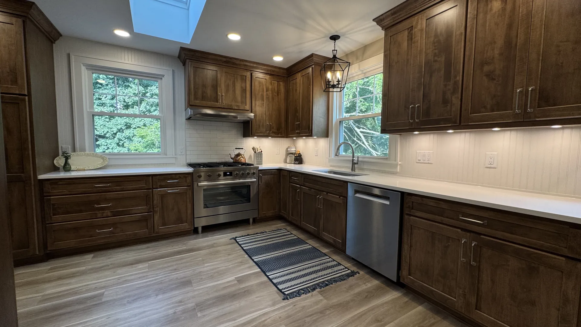 Renovated L-shaped kitchen with dark cabinets, white backsplash, stainless range and dishwasher, and skylight overhead.