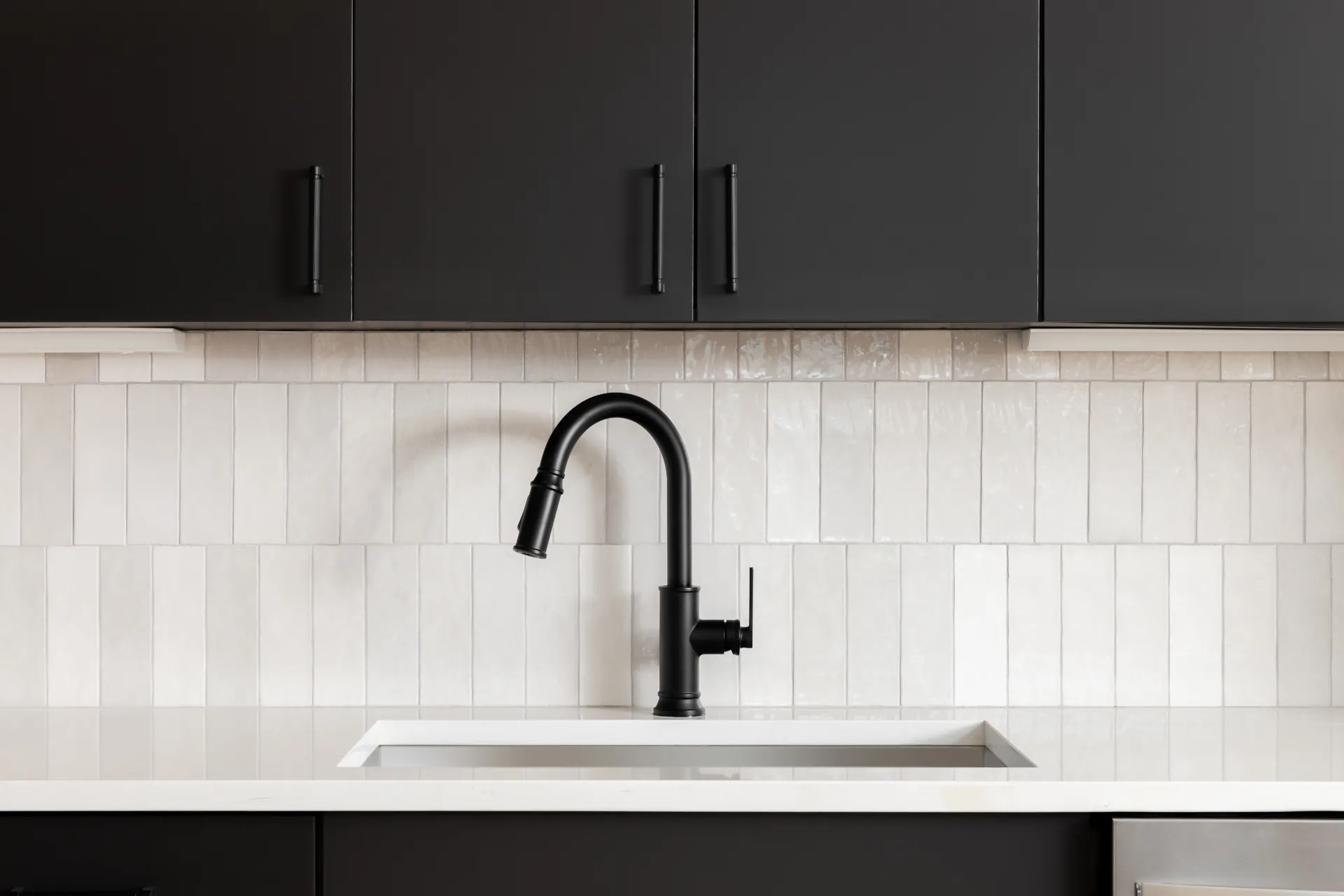 white tile backsplash behind a sink with black cabinets on top and bottom