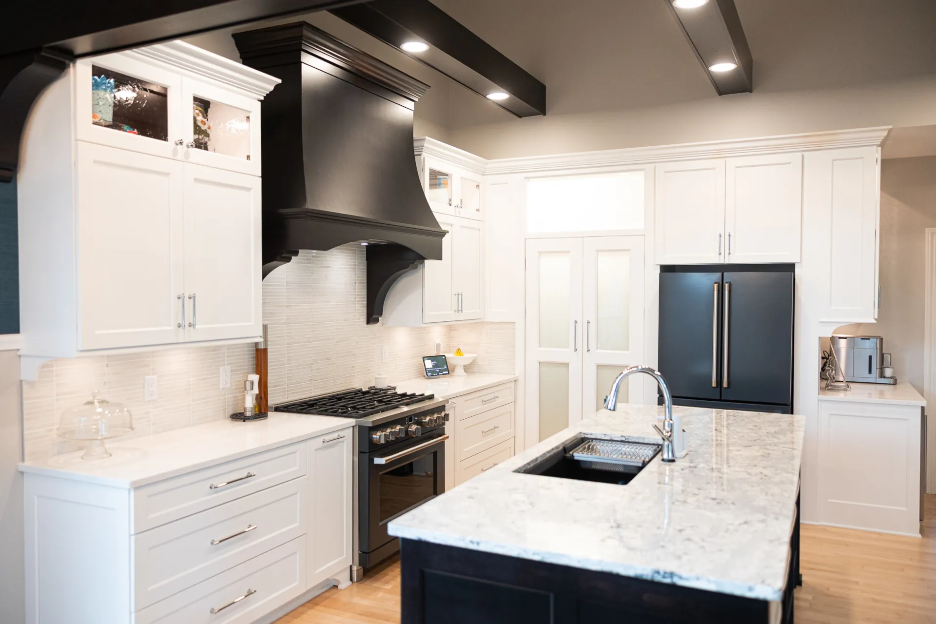 Remodeled kitchen with custom white cabinetry, dark island, quartz countertops, custom wood range hood, and ceiling beams.