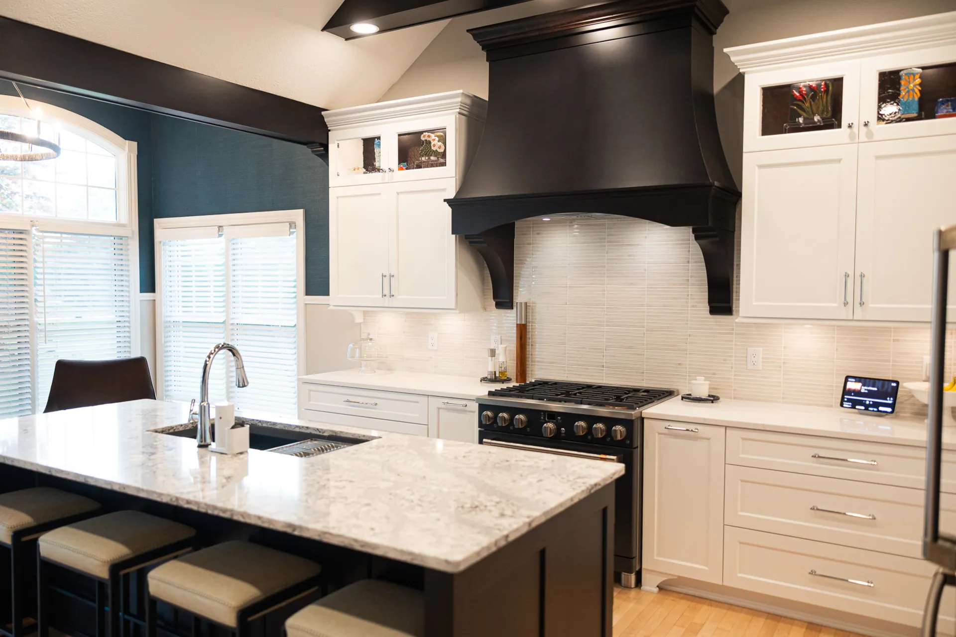 Custom kitchen remodel with white cabinetry, dark wood range hood, large island with seating, and quartz countertops.