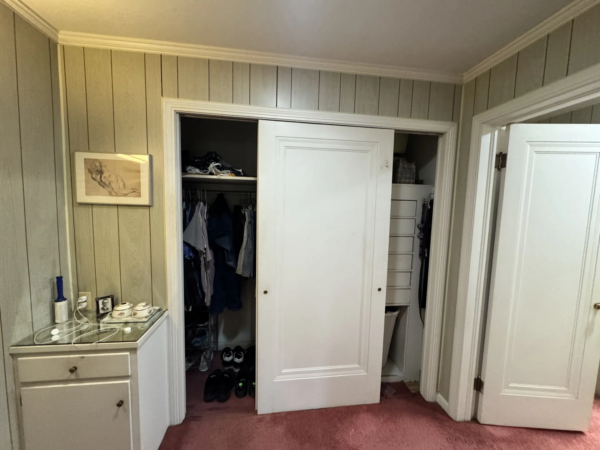 Primary bathroom before remodeling with an outdated closet, wall paneling, and limited storage.