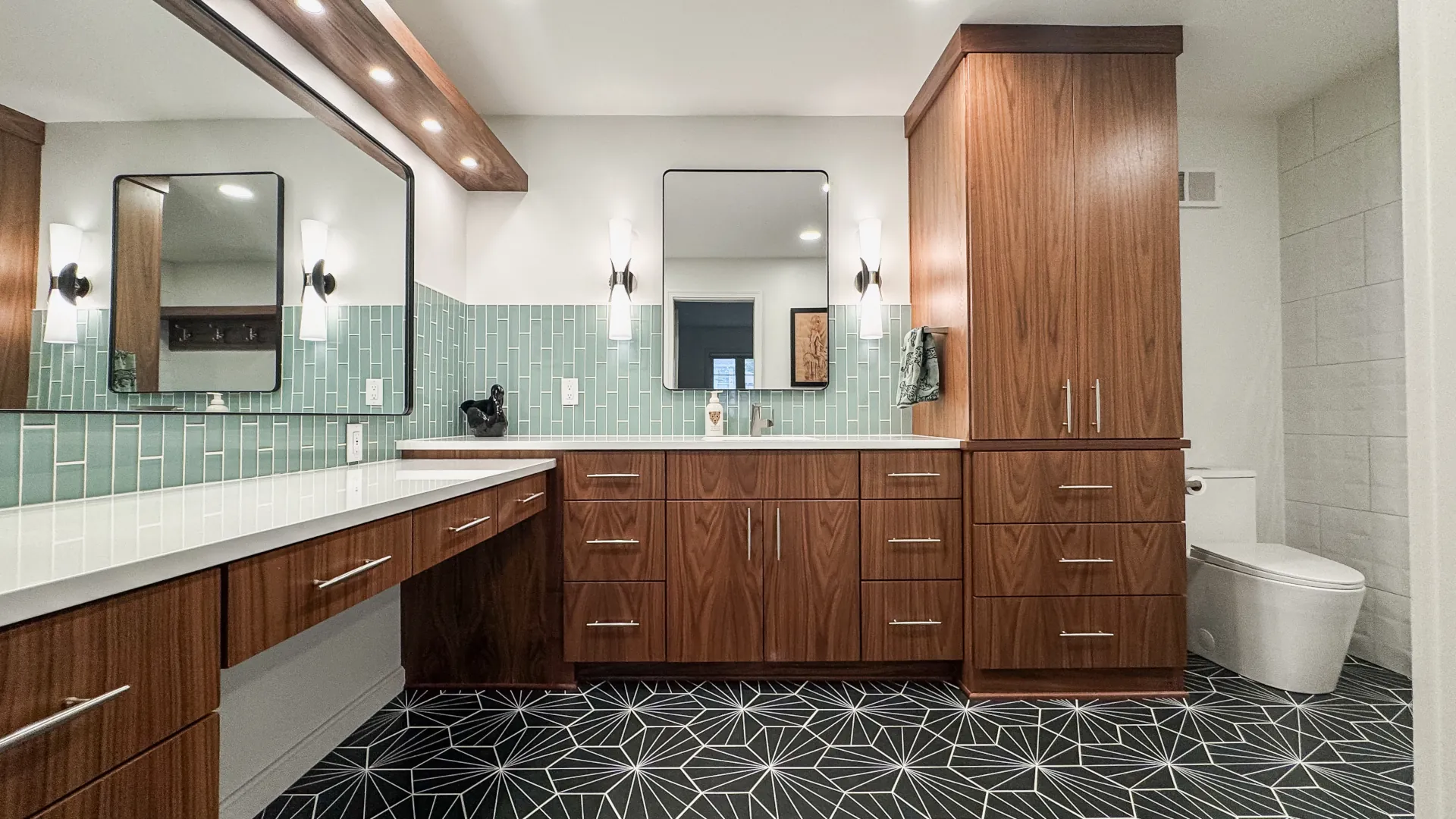 Remodeled primary bathroom with custom walnut cabinetry, floating makeup vanity, quartz countertops, geometric floor tile, and modern lighting.