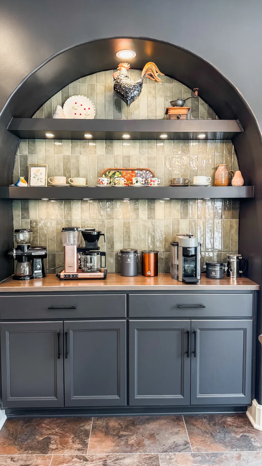Custom arched coffee bar with dark cabinetry, open shelving, integrated lighting, and textured green tile backsplash.