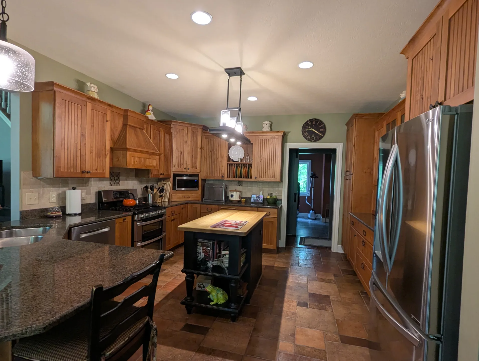 Kitchen before renovation with wood cabinetry, small center island, granite countertops, and stainless steel appliances.