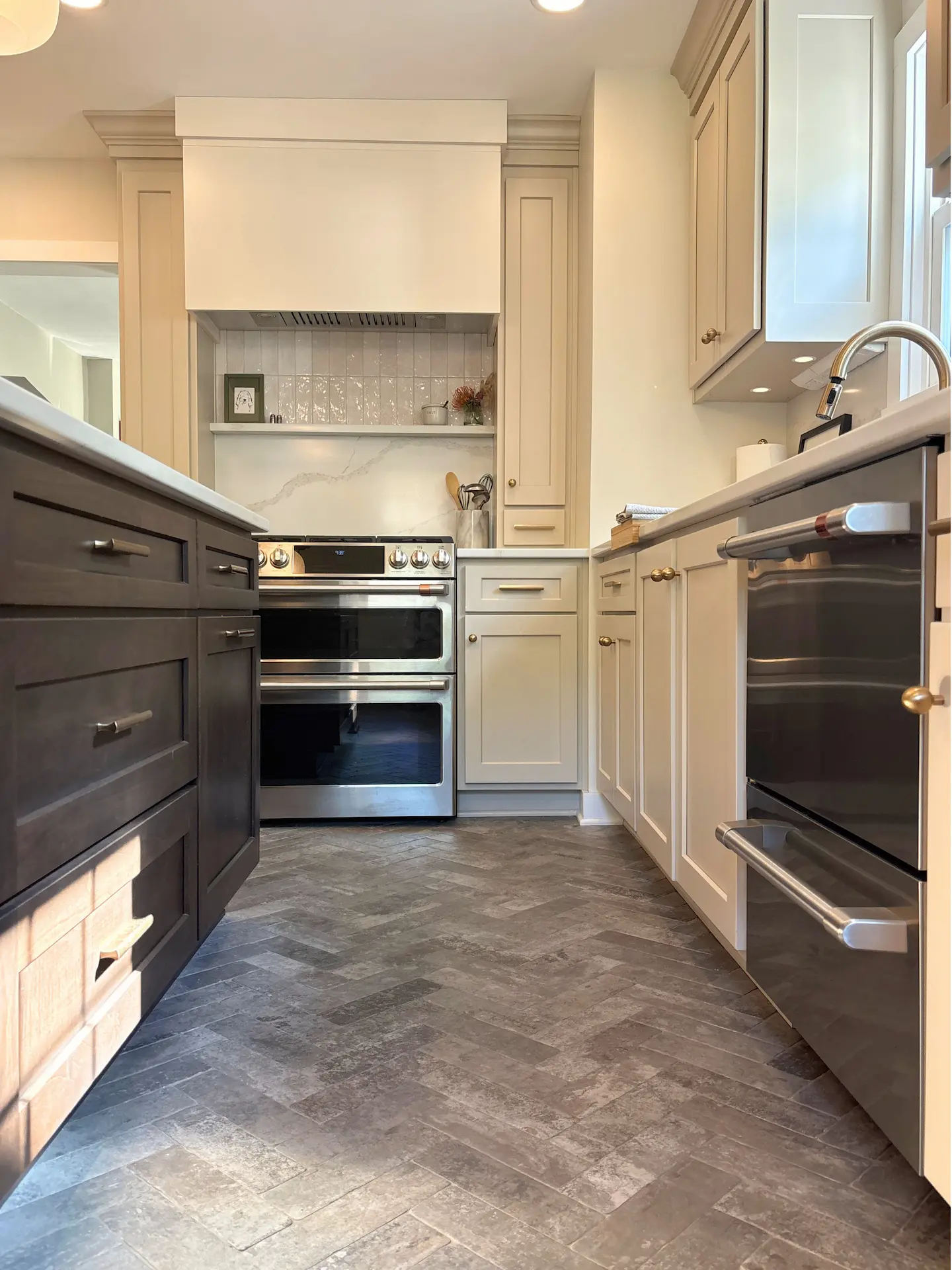 Remodeled kitchen with two-tone cabinetry, stainless steel appliances and herringbone tile flooring