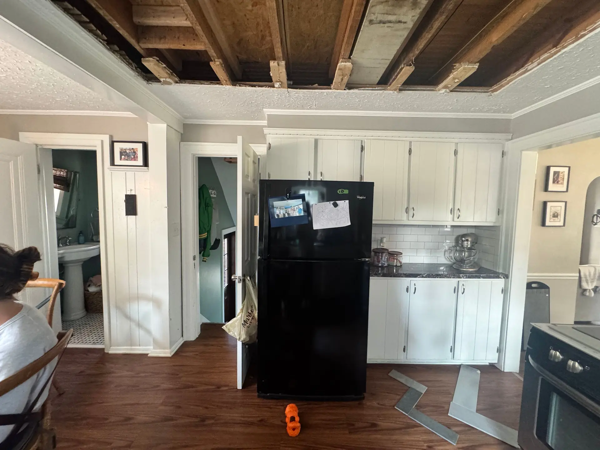 Kitchen before renovation with white cabinetry, black refrigerator and exposed ceiling joists