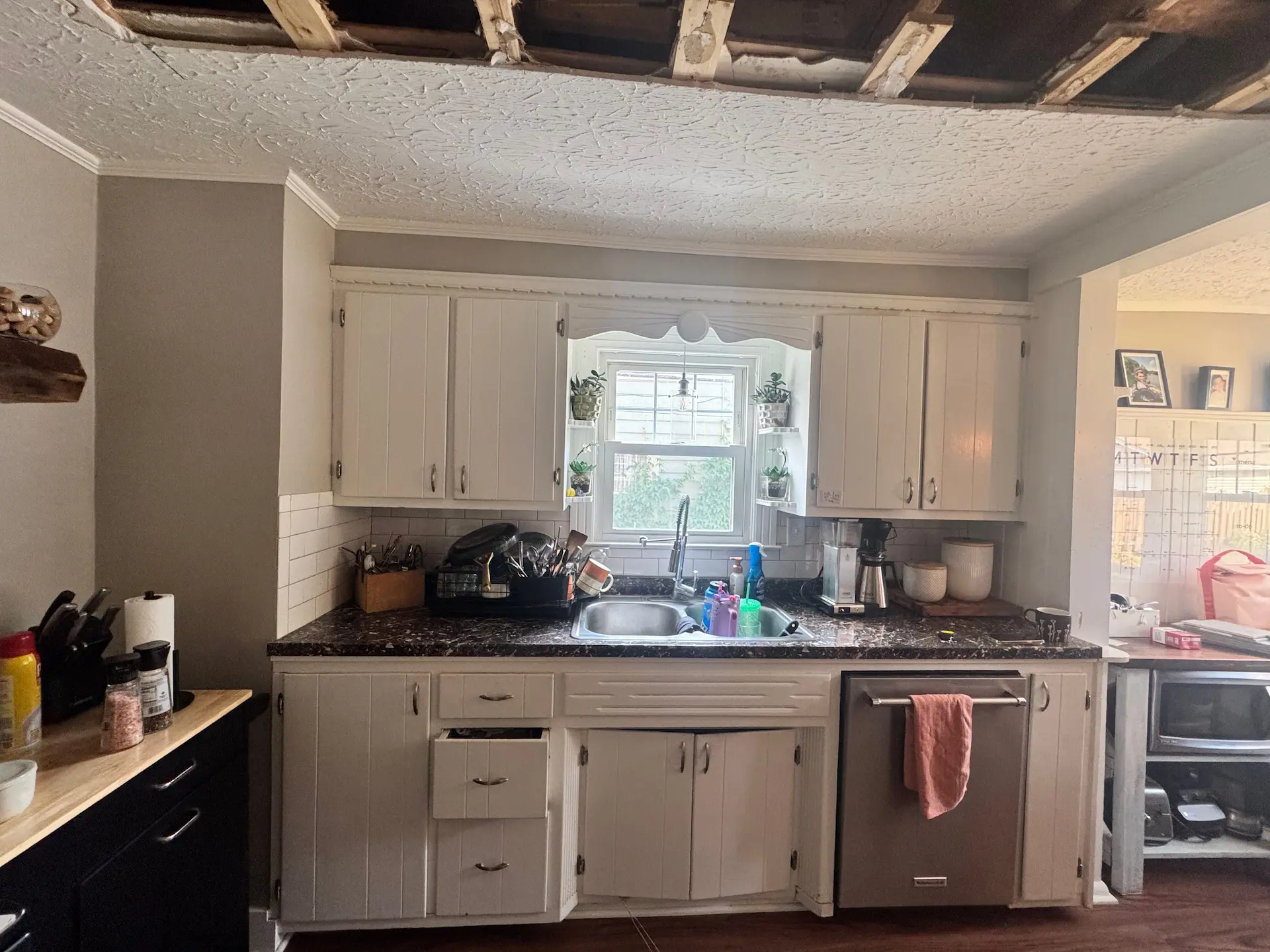 Kitchen before remodeling with white cabinets, dark countertops and partially removed ceiling