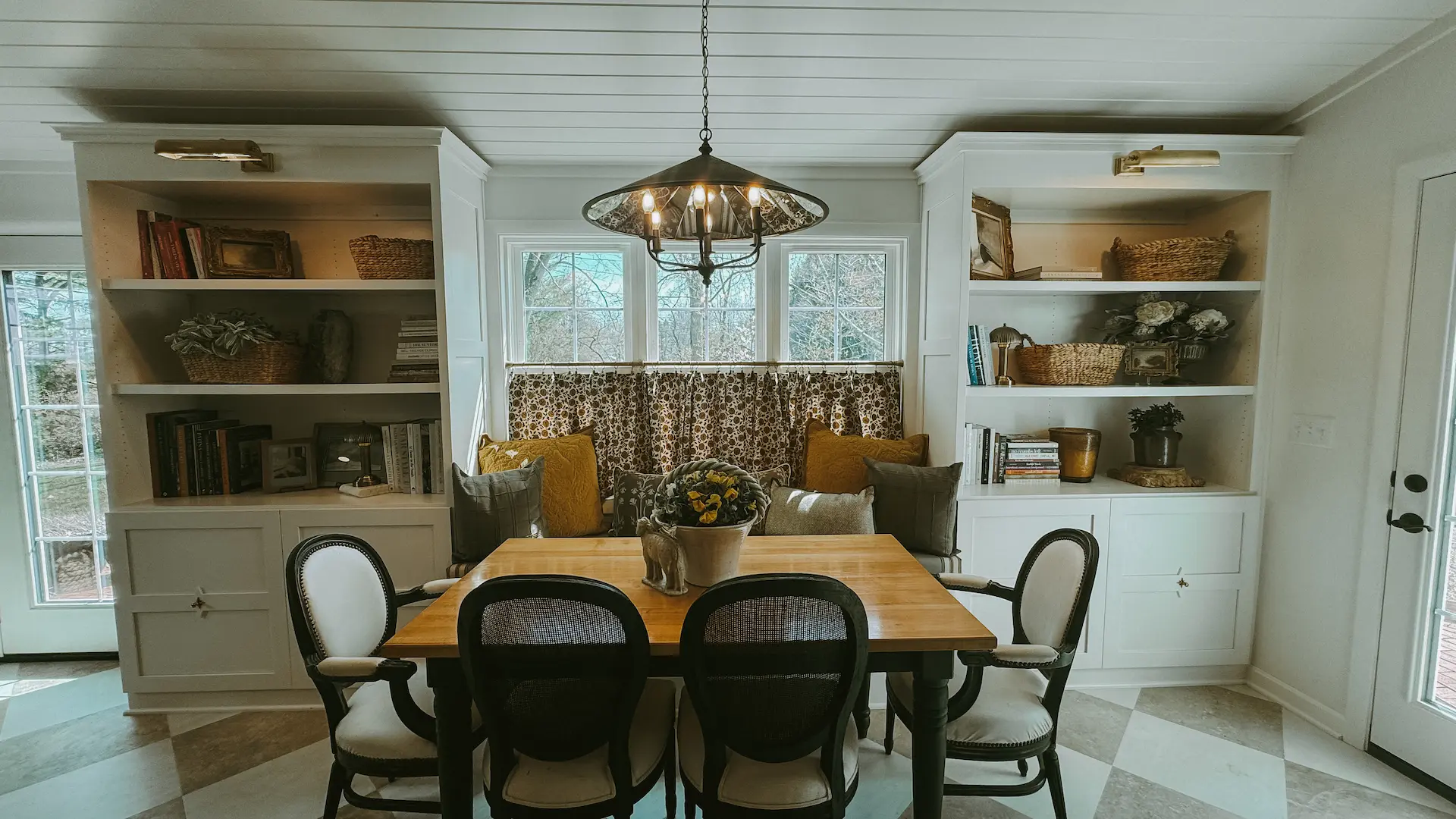 Cozy gathering area with built-in shelving, window seating, café curtains and checkerboard flooring