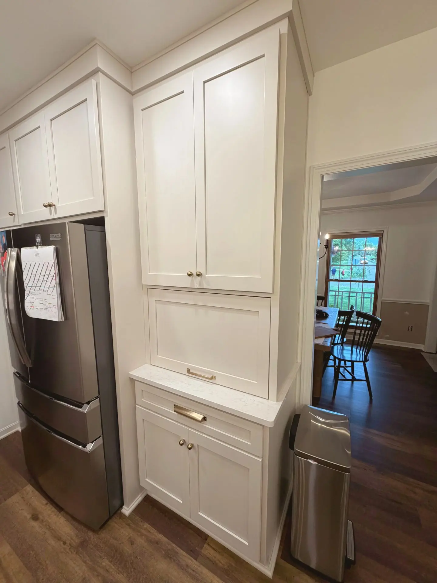Full-height white custom kitchen cabinetry with built-in storage beside stainless steel refrigerator