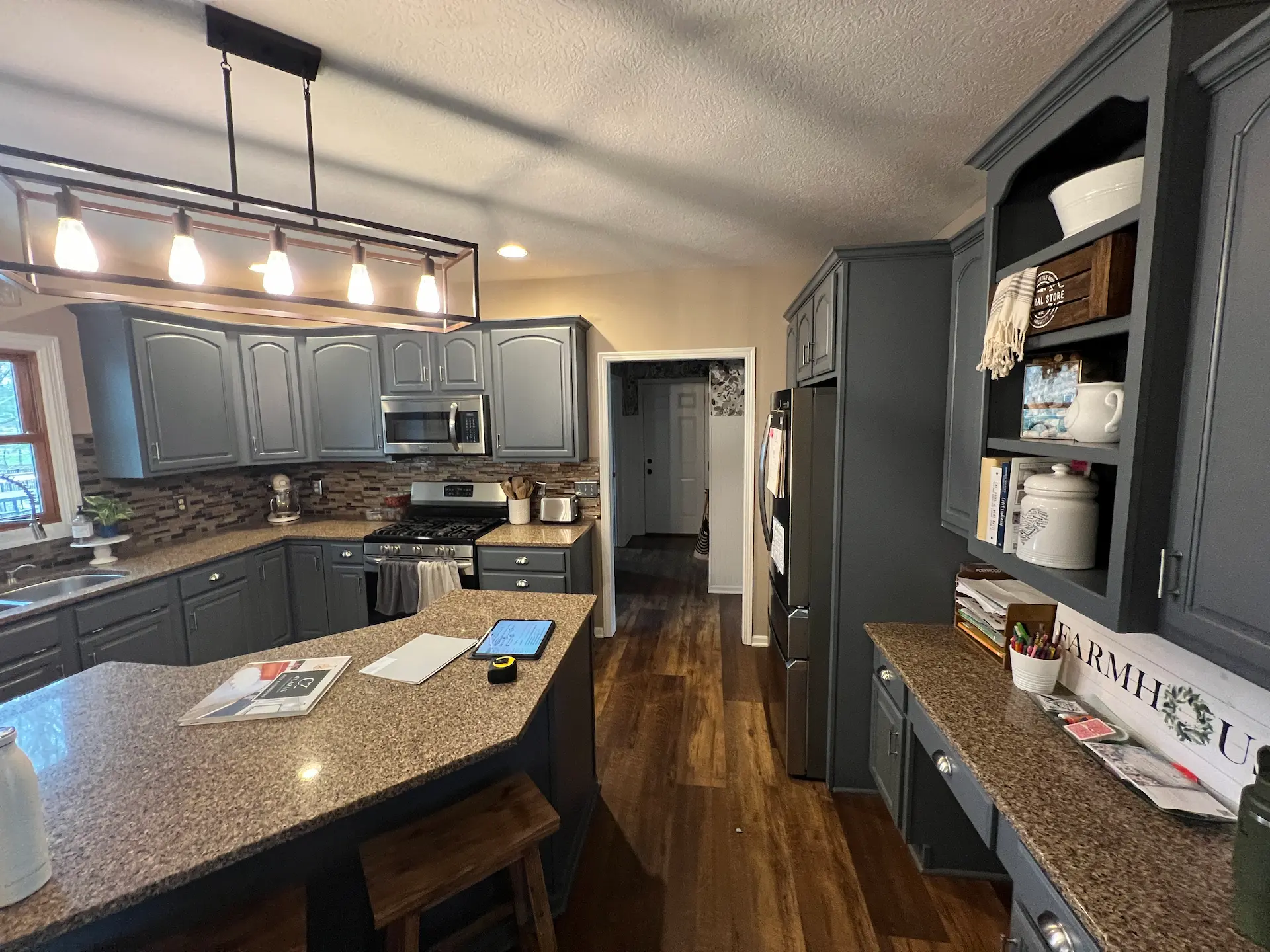 Kitchen before remodel with gray cabinets, granite island and built-in open shelving