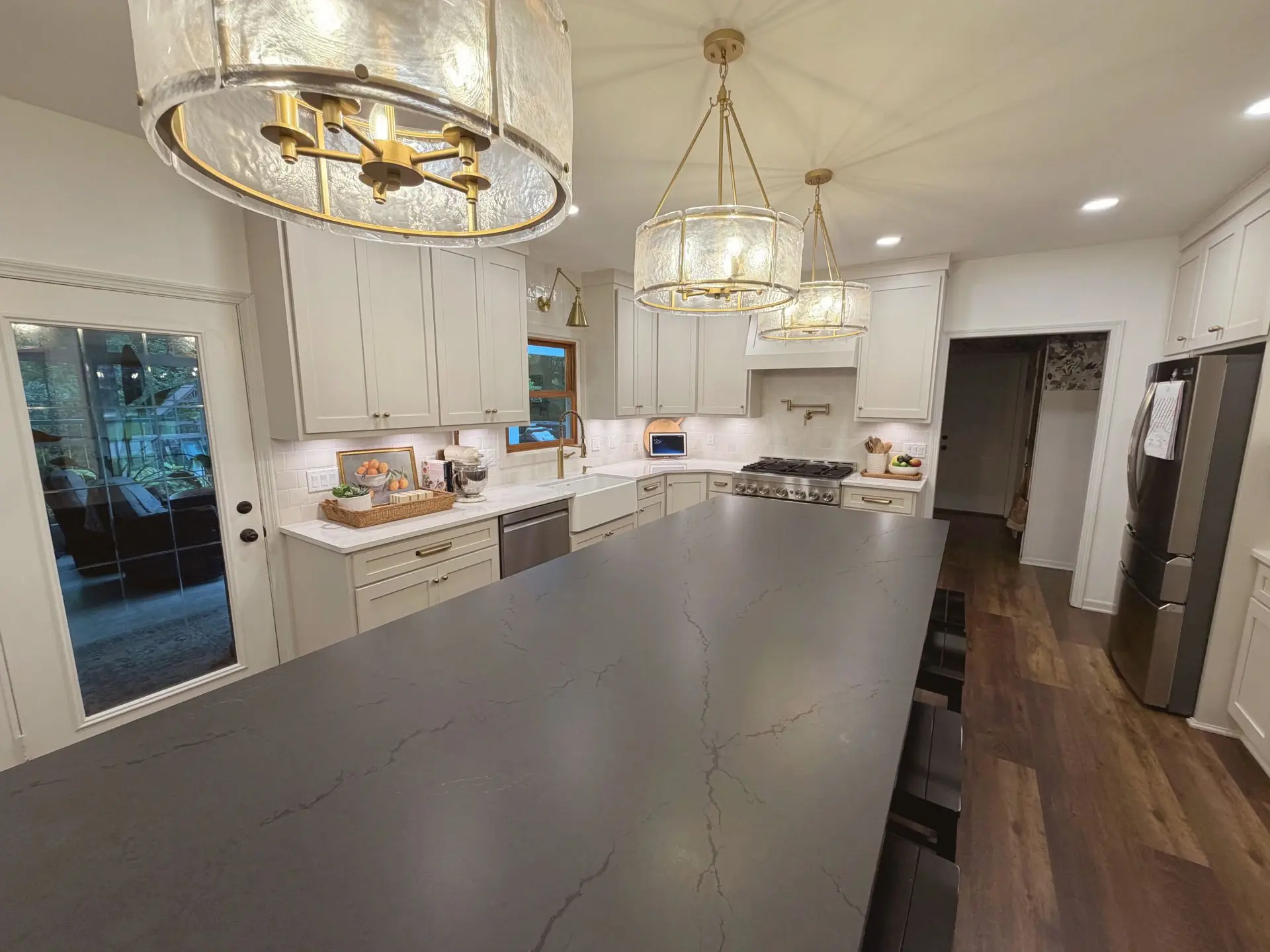 Remodeled kitchen with white cabinetry, large contrasting island, apron-front sink and pendant lighting