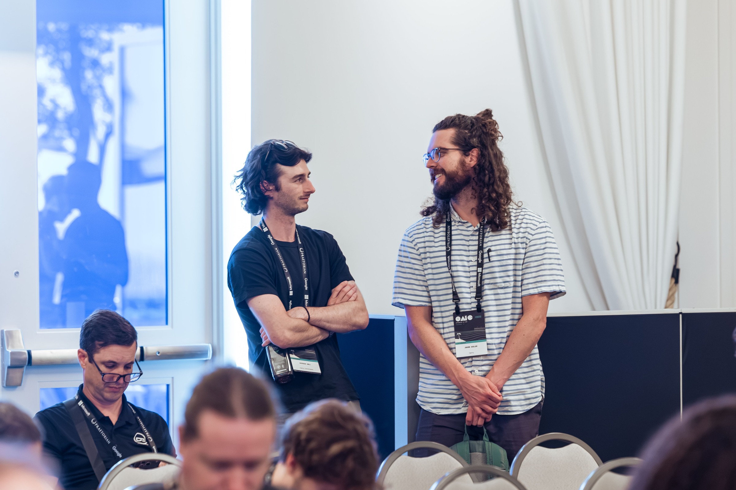 Two attendees talking together near the wall of the conference room during a break.