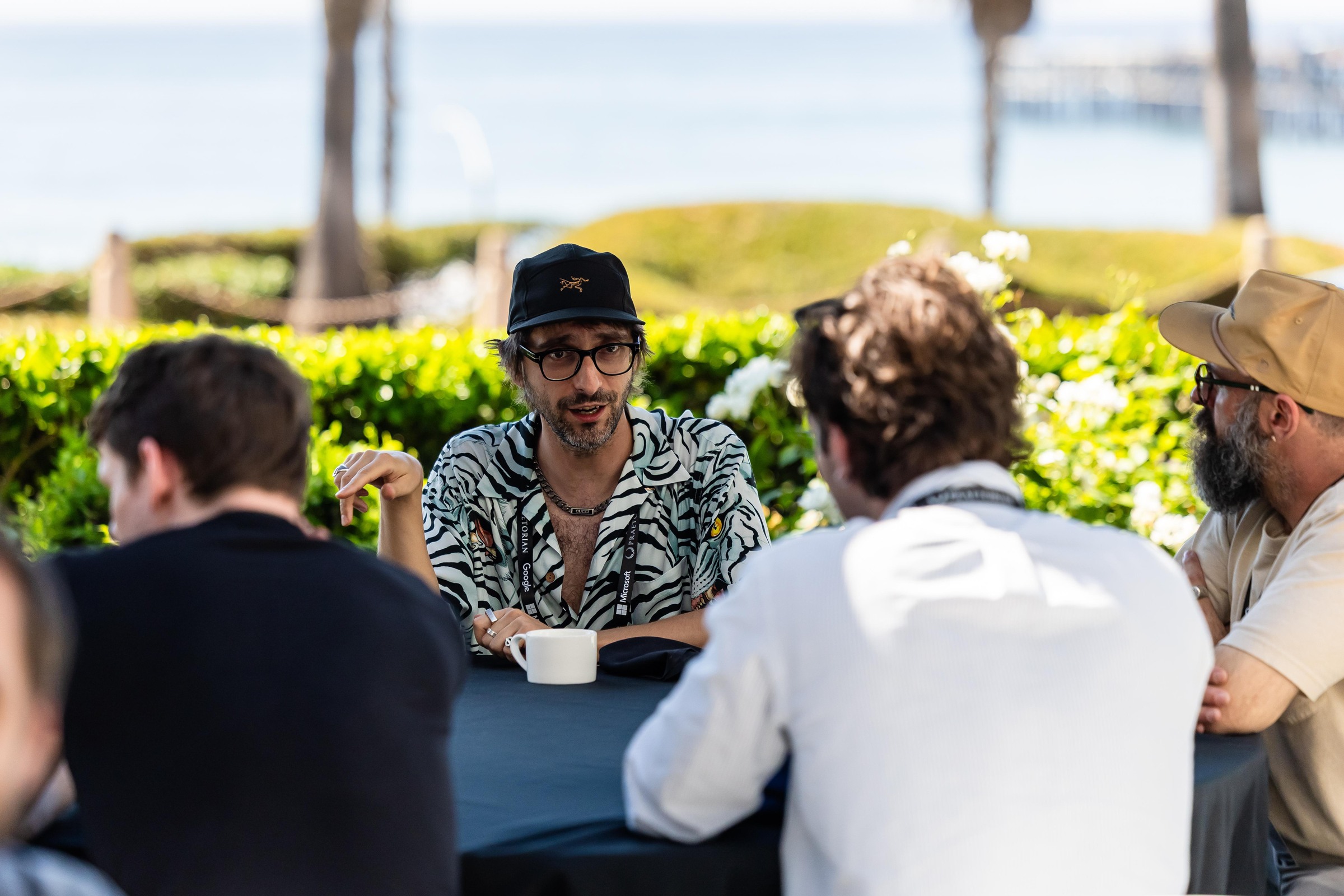 Attendees discussing ideas around an outdoor lunch table with the ocean behind them.