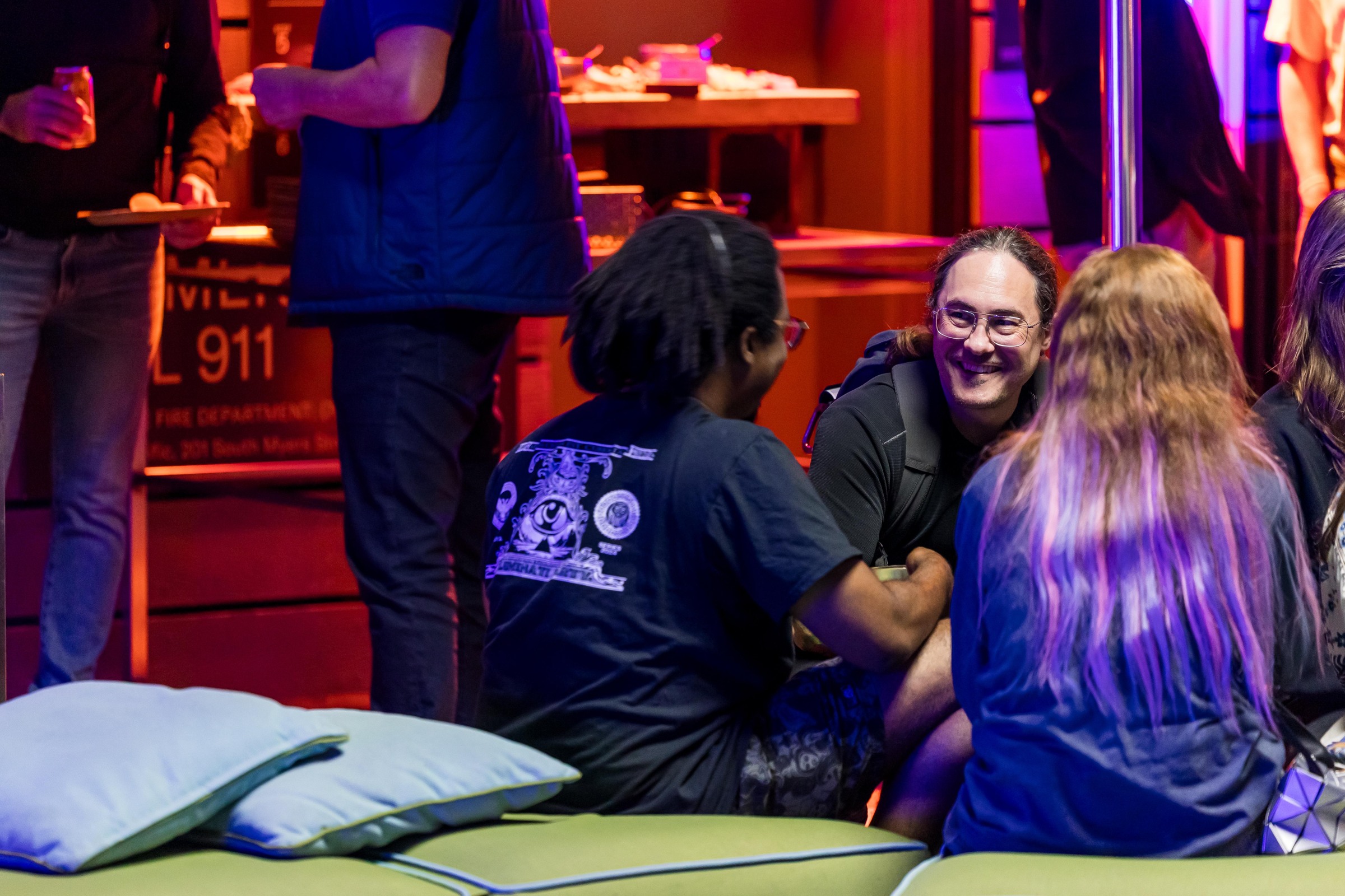 Three attendees smiling and talking on the lounge seating at the Monday gathering.