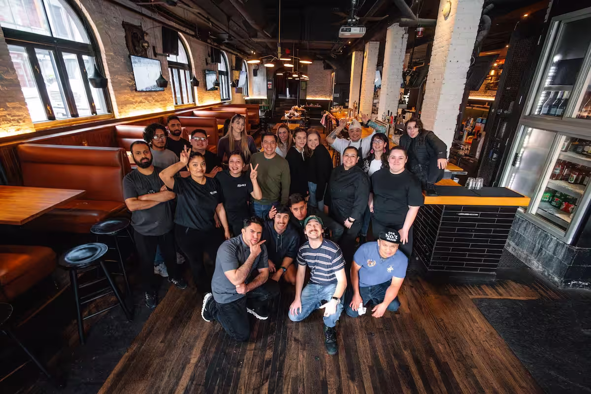 Smiling diverse group of people posing inside a cozy restaurant with wooden floors and booths.
