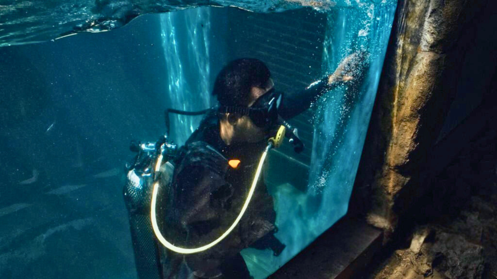 Pool technician inspecting underwater window for leaks and scratches