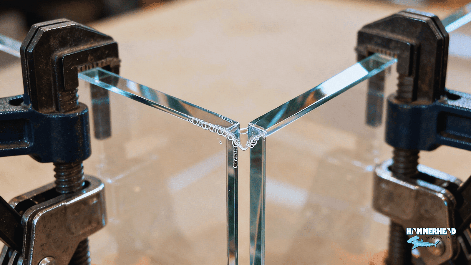 Macro of capillary acrylic bonding seam with clamps and polished edges during aquarium window setup.