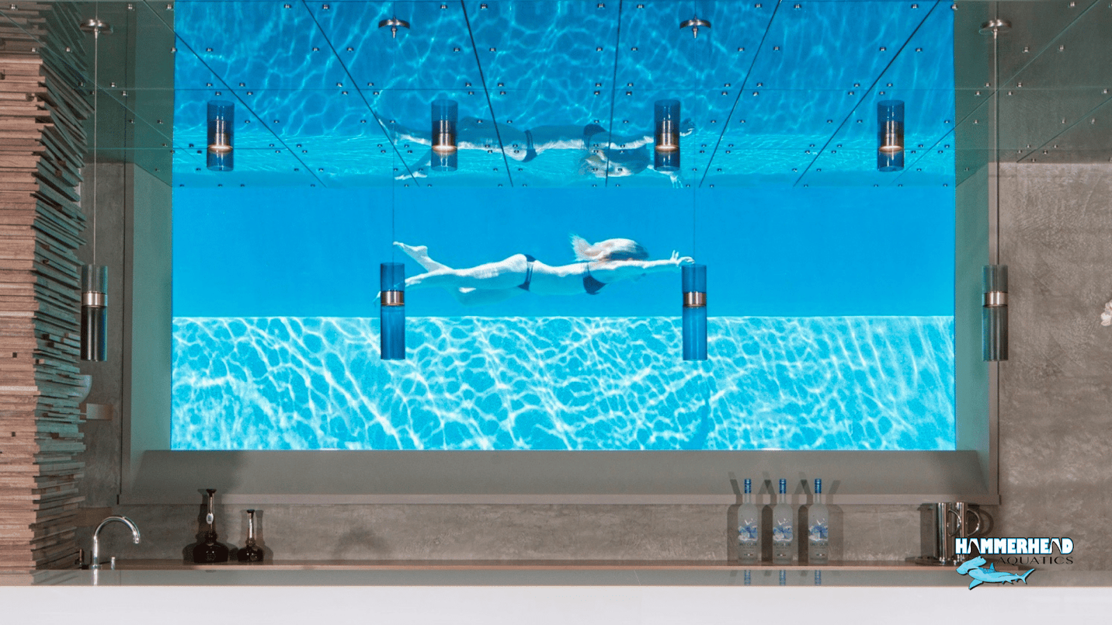 A woman is swimming seen  through an underwater window in a tiled pool.