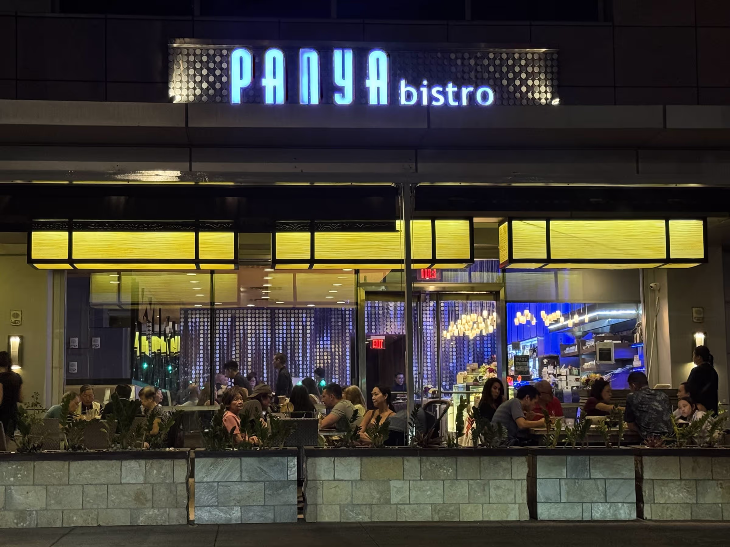 The facade of a restaurant at night, with warm lights and a sign.