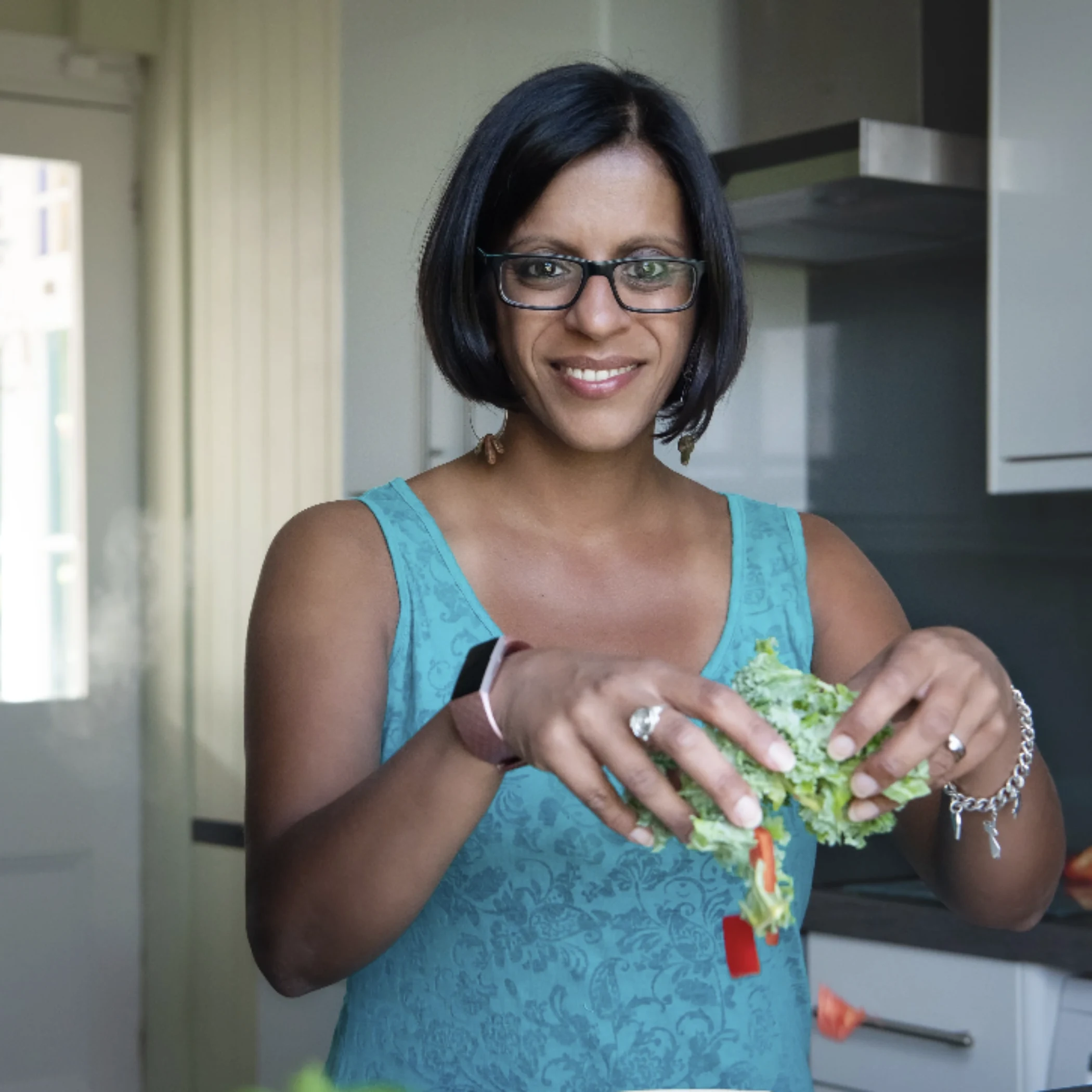 Woman in turquoise tank top tearing fresh lettuce over a kitchen counter.
