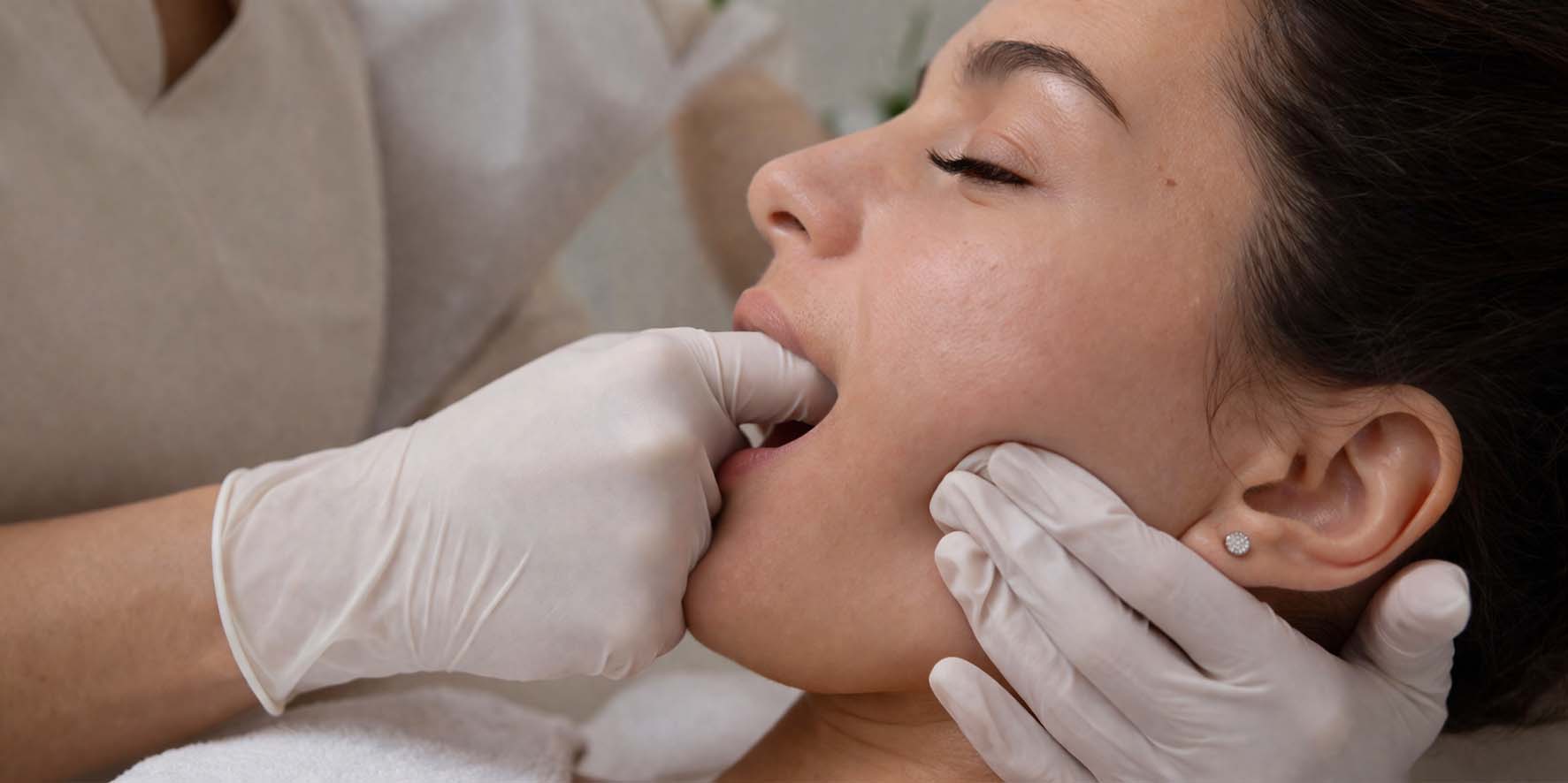 Therapist's gloved fingertips working along a client's cheek during a buccal facial massage